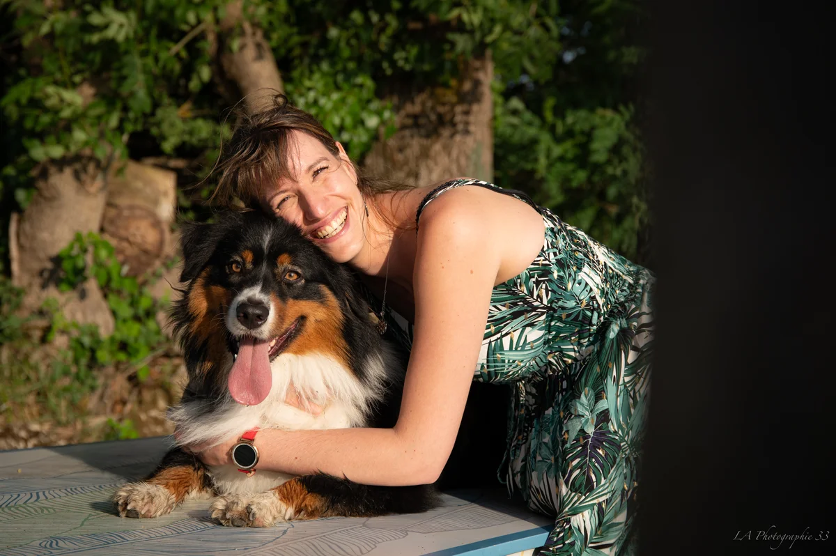 Femme souriante tenant dans ses bras un bouvier bernois, assise en extérieur