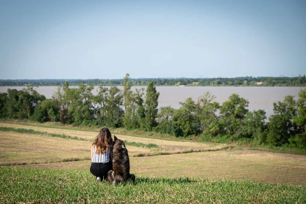 Jeune femme de dos assise avec son chien face à un fleuve