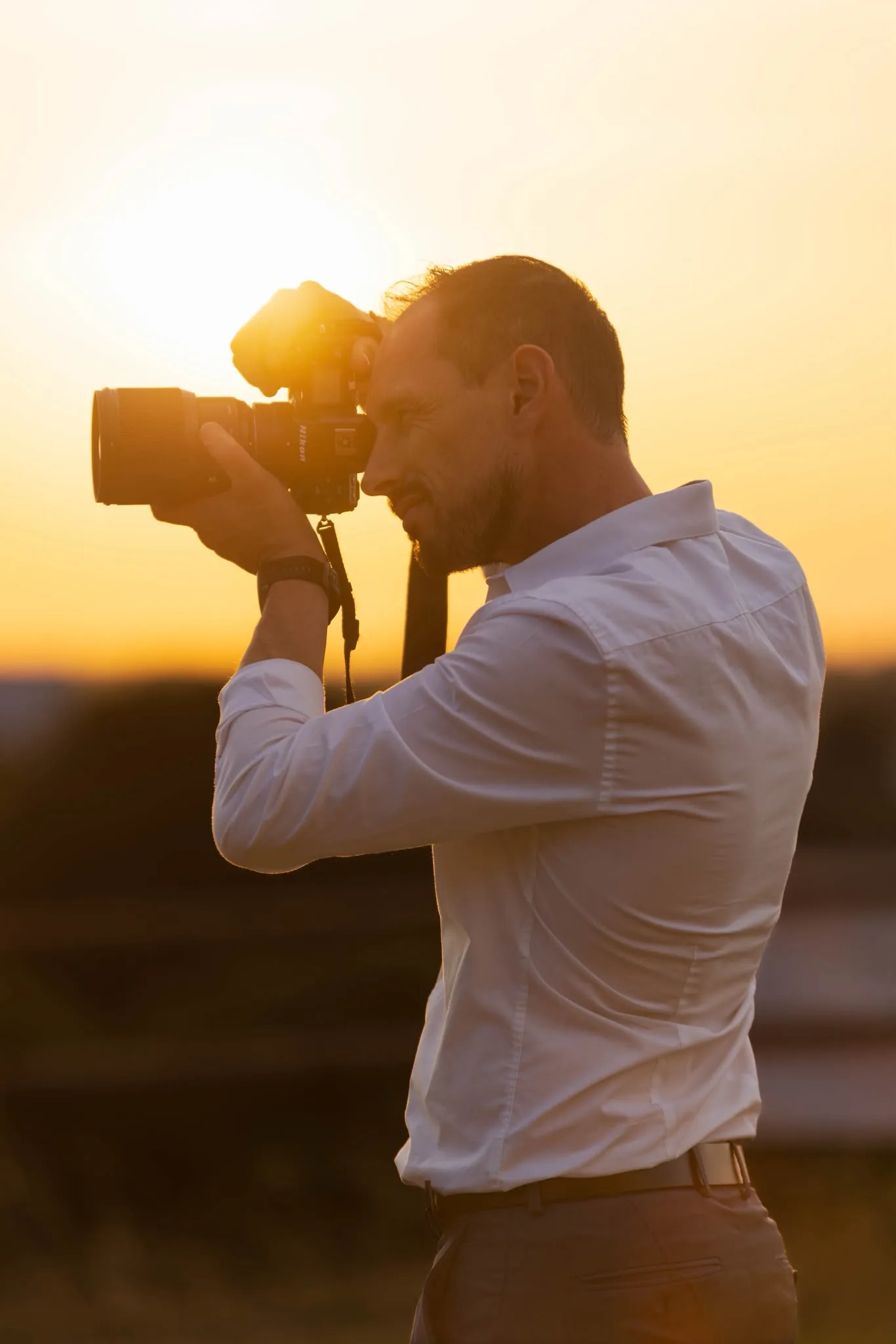 Aurélien Lambert, photographe, appareil photo à l'épaule, éclairé en contre-jour par la lumière dorée du soleil