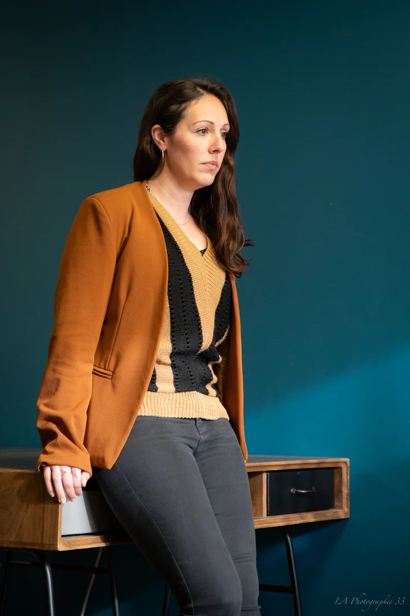 Femme en veste orange posant contre un mur bleu dans un intérieur élégant