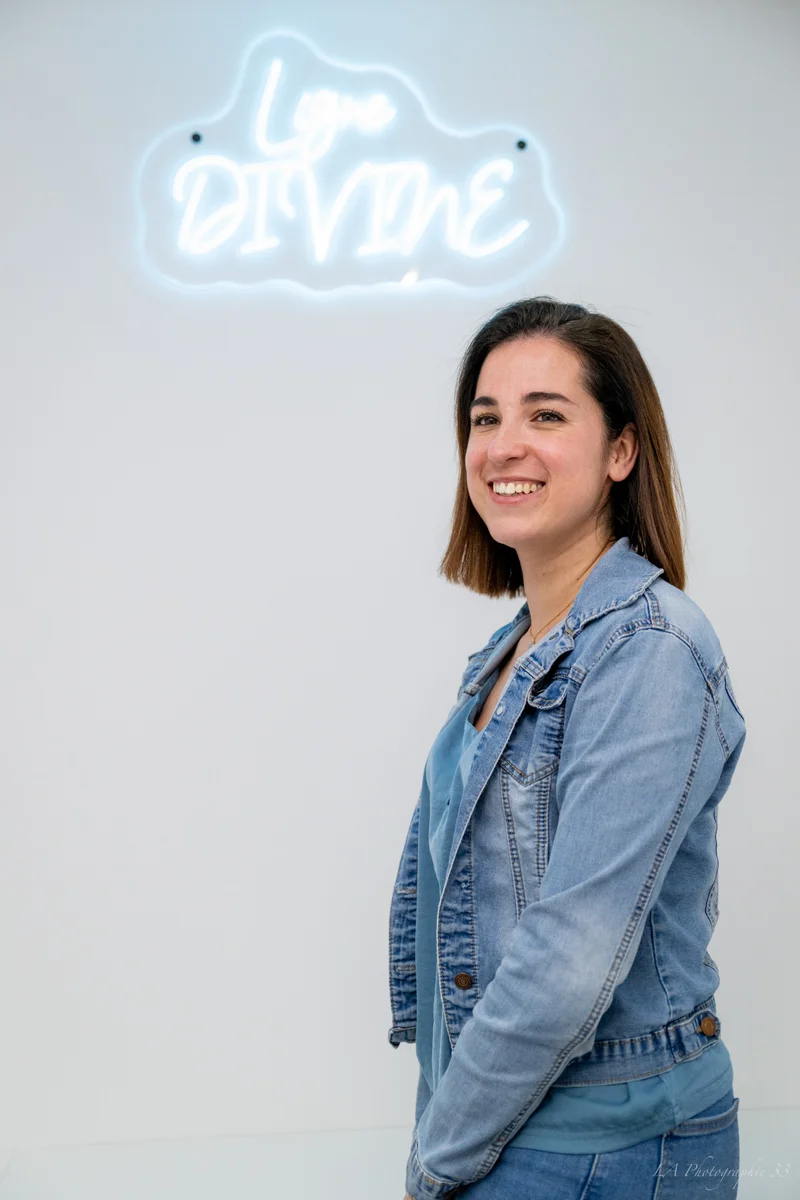 Femme souriante posant devant une enseigne lumineuse 'Love Divine'