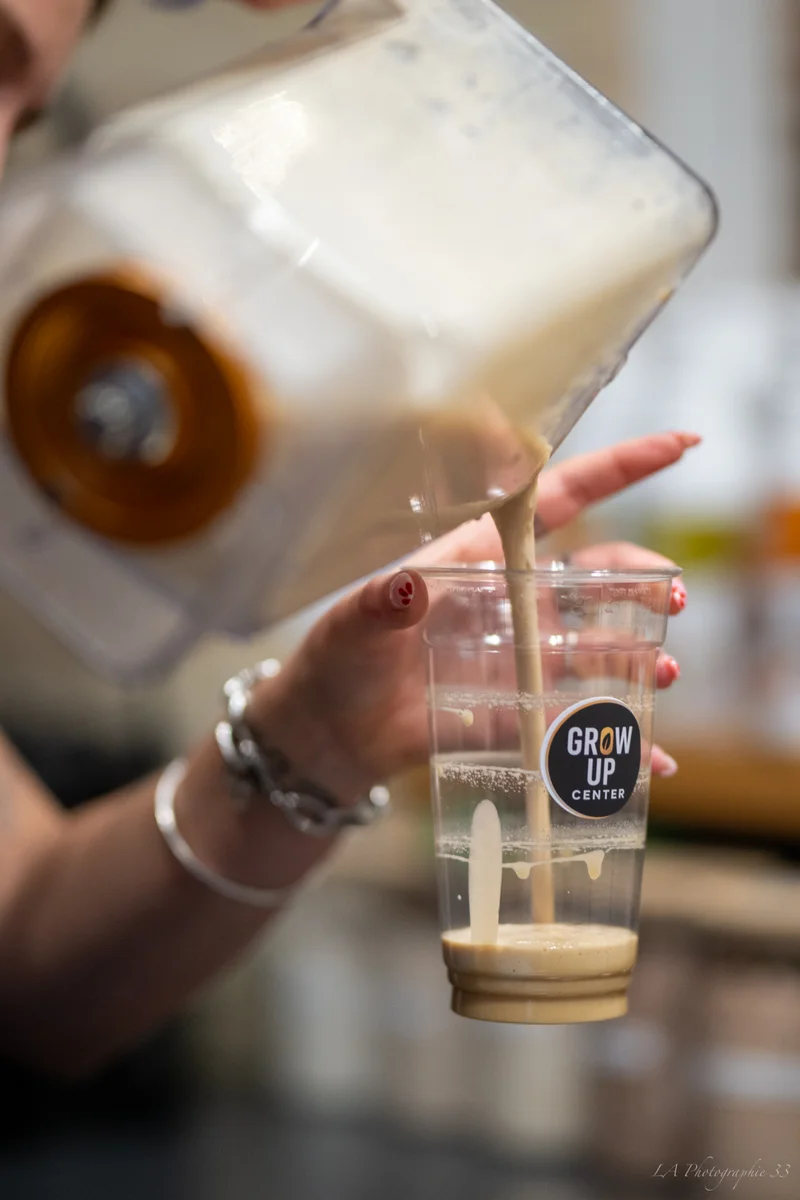 Mains versant une boisson dans un verre en plastique transparent avec un logo 'Grow Up Center'