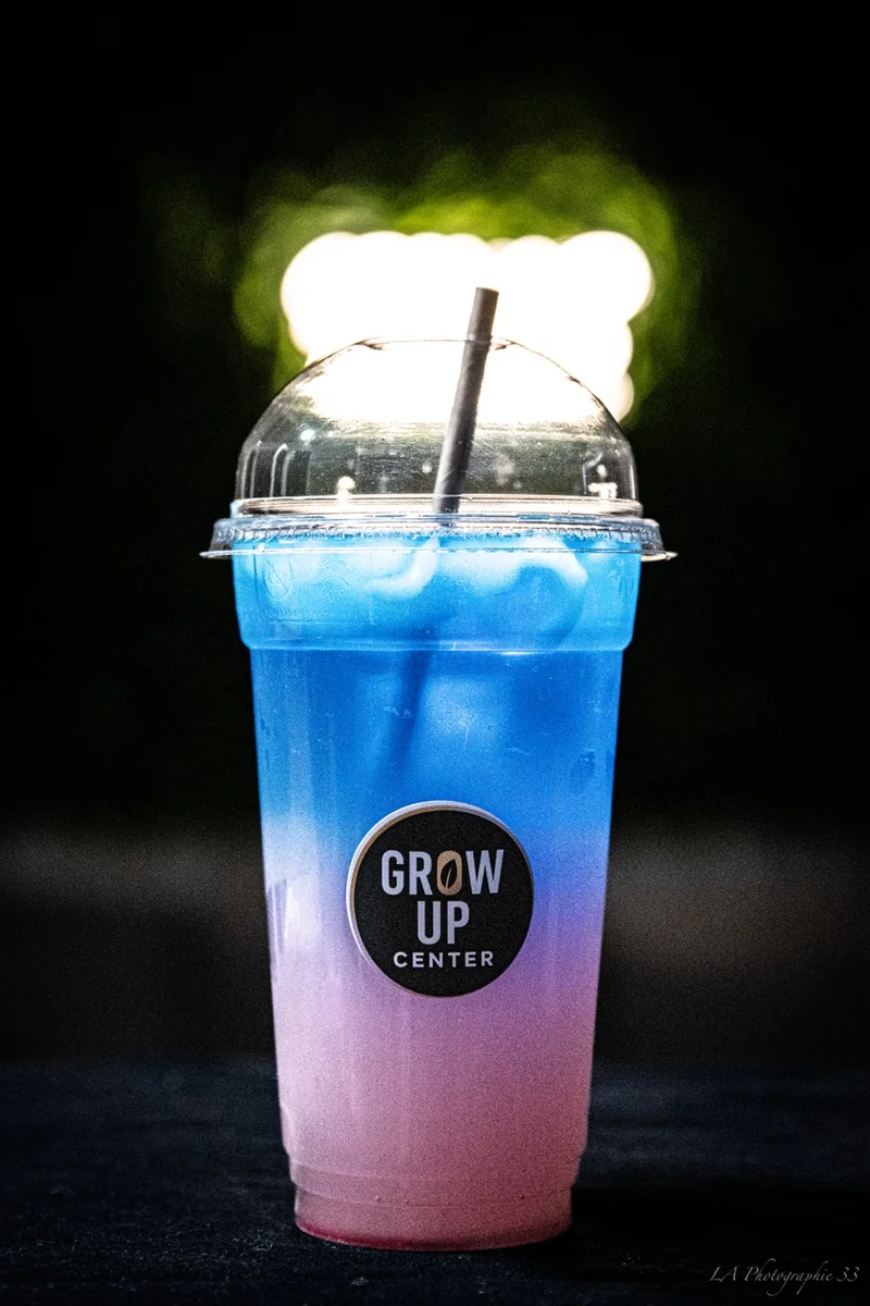 Boisson colorée avec logo 'Grow Up Center' photographiée en gros plan sur fond sombre
