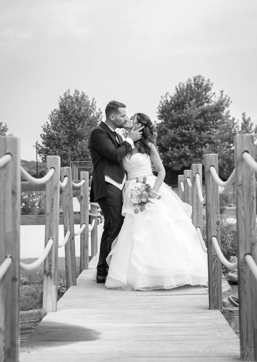 Photo en noir et blanc de mariés s'embrassant sur une passerelle en bois