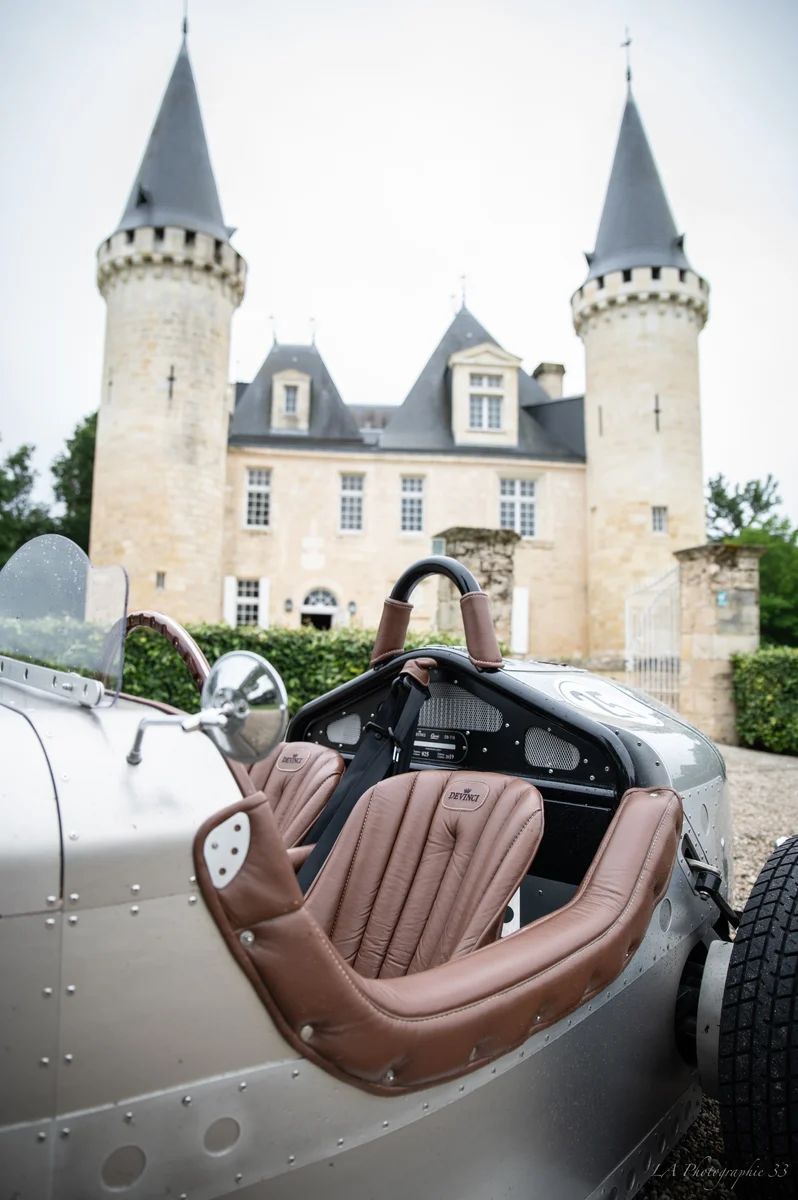 Voiture de course vintage aux sièges en cuir devant un château à tourelles