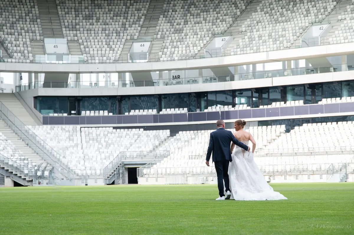 Les mariés de dos, bras dessus bras dessous, traversant la pelouse d'un stade