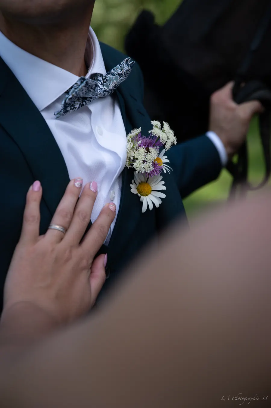 Gros plan sur la boutonnière fleurie du marié, main de la mariée posée sur son torse