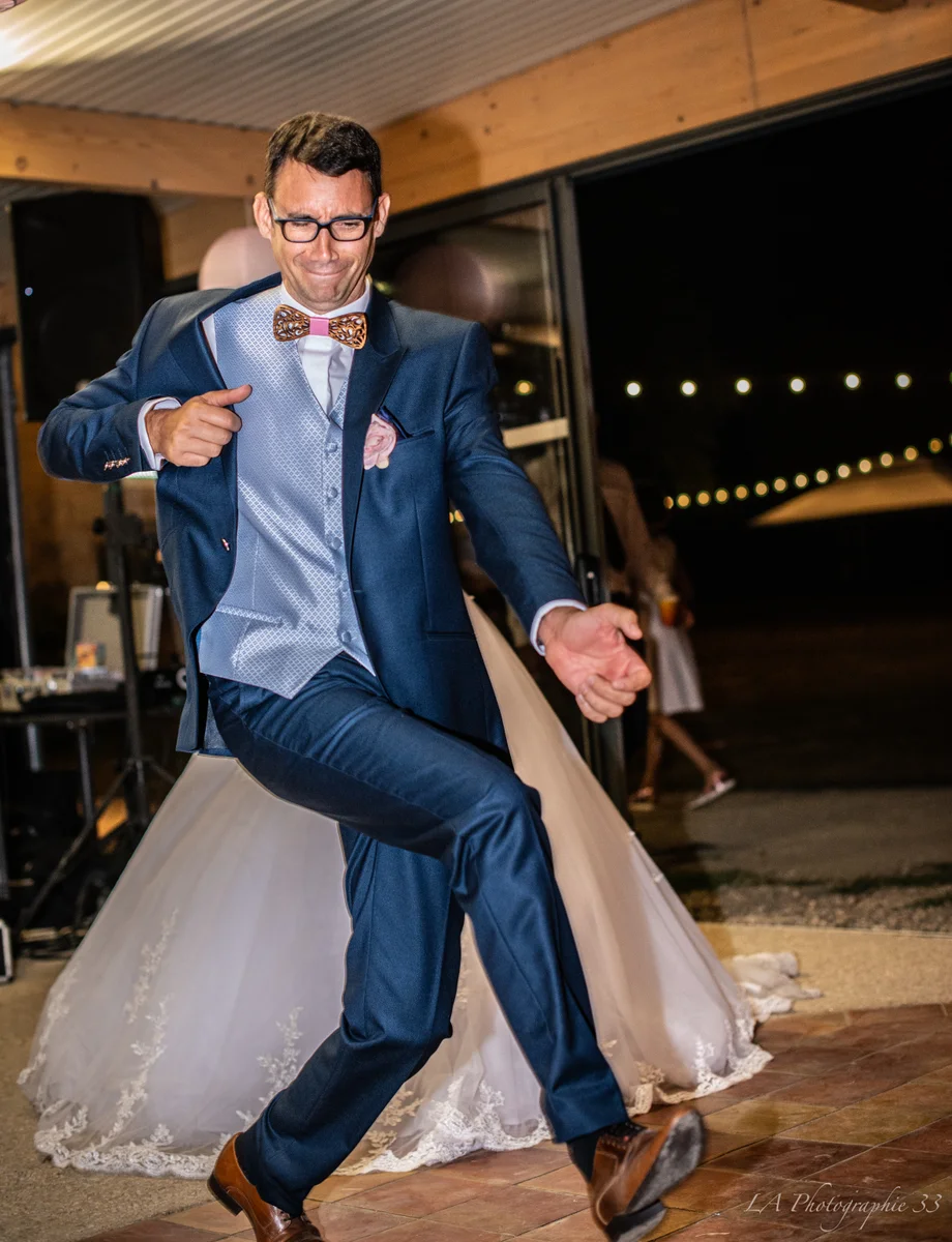 Marié dansant avec entrain lors de la soirée, robe de la mariée en arrière-plan