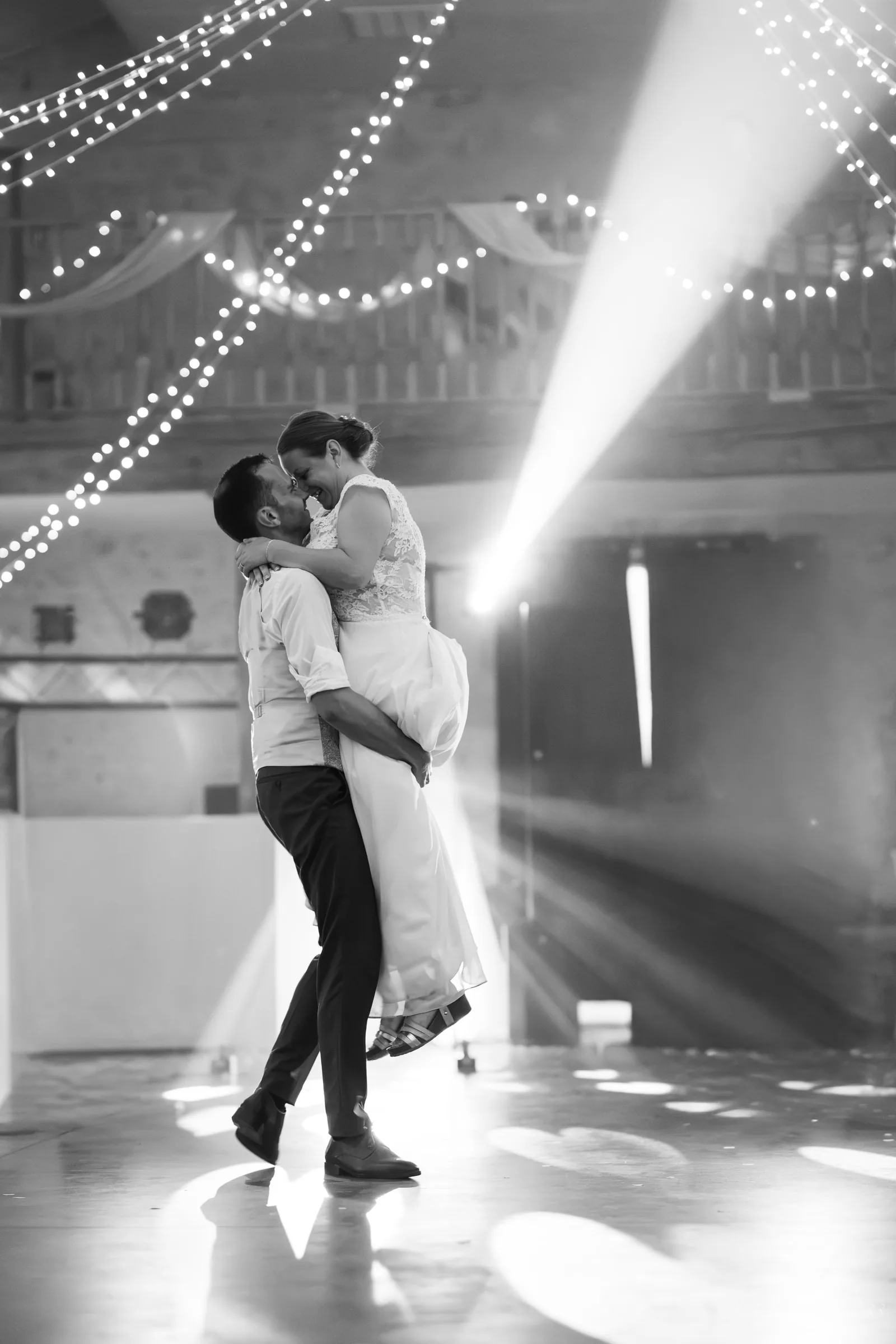 Les mariés enlacés sur la piste de danse sous les guirlandes lumineuses, en noir et blanc