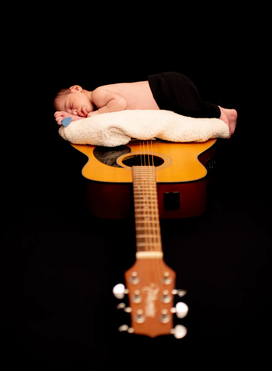 Nouveau-né endormi sur une guitare acoustique, coiffé d'un bonnet noir