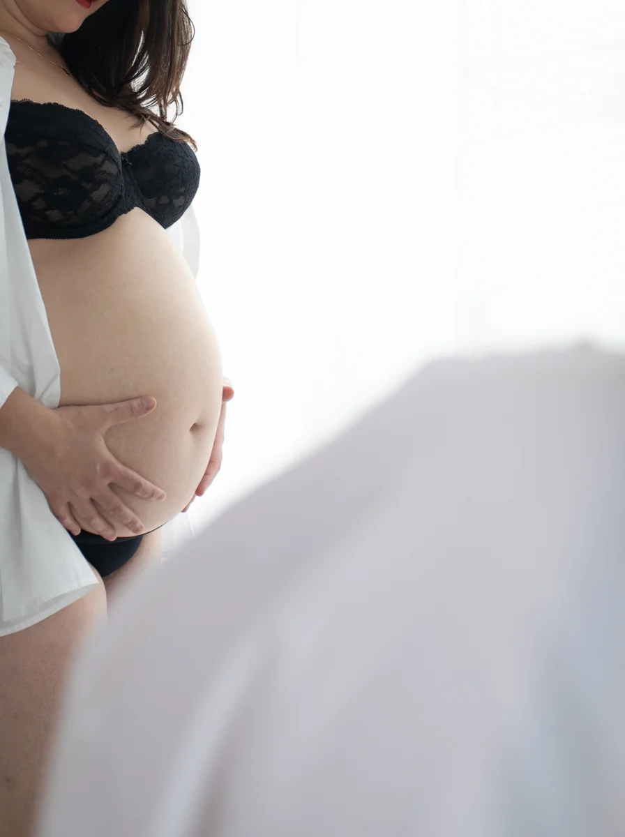 Gros plan sur un ventre de femme enceinte en lingerie noire, chemise blanche entrouverte