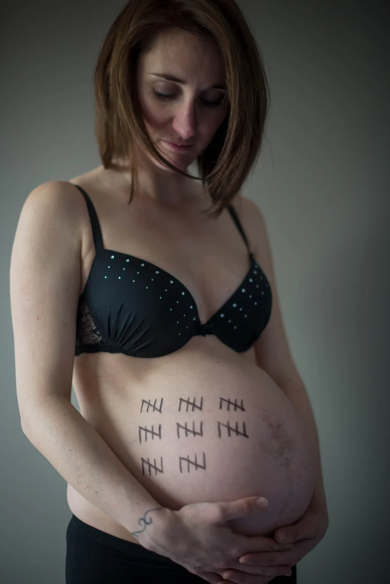 Femme enceinte en sous-vêtements noirs, décompte des semaines tracé sur le ventre