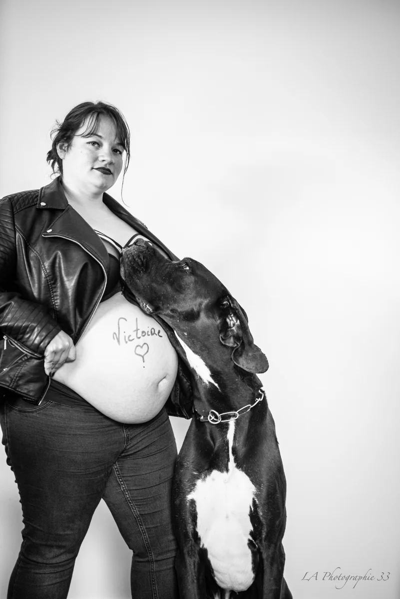 Photo en noir et blanc d'une femme enceinte en veste en cuir avec son chien géant