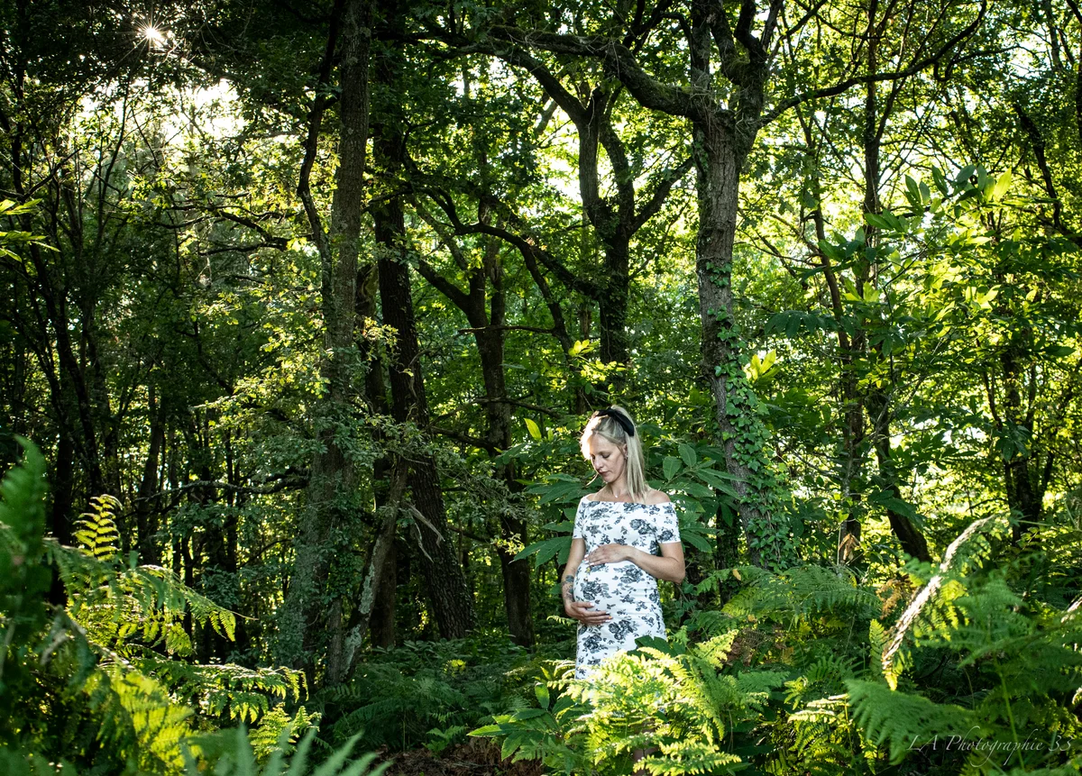 Femme enceinte en robe fleurie tenant son ventre au milieu d'une forêt de fougères