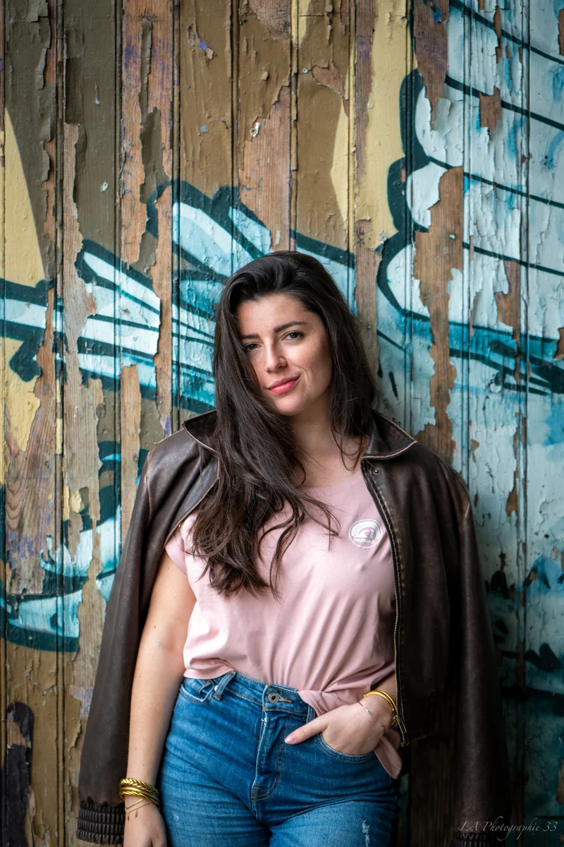 Portrait d'une jeune femme brune devant un mur de bois peint et tagué