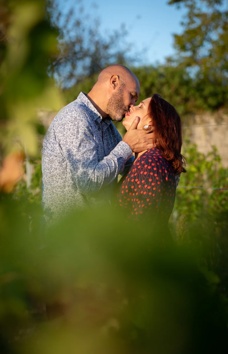 Couple s'embrassant dans les vignes au coucher de soleil, vu à travers des feuilles